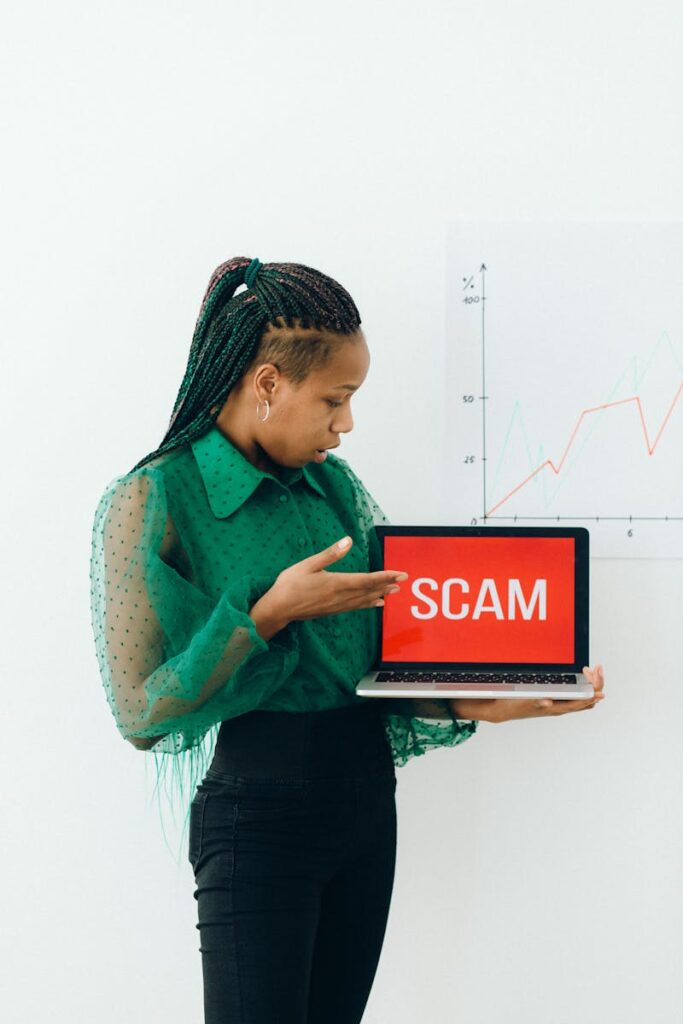 Woman in green pointing at laptop showing 'SCAM' sign, highlighting online scam awareness.