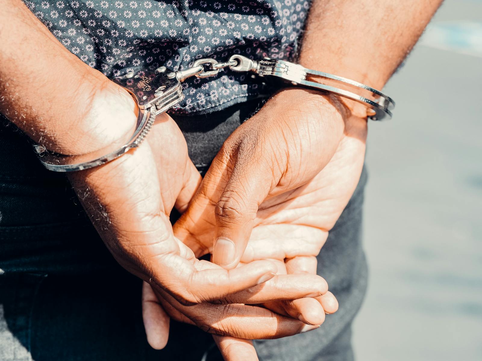 Close-up of an adult male's hands in handcuffs, symbolizing law enforcement and justice.