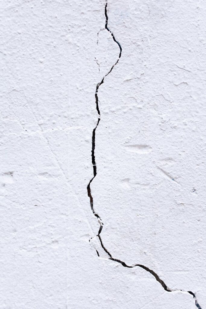 Textured background of rough uneven surface with cracks and scratches on white wall