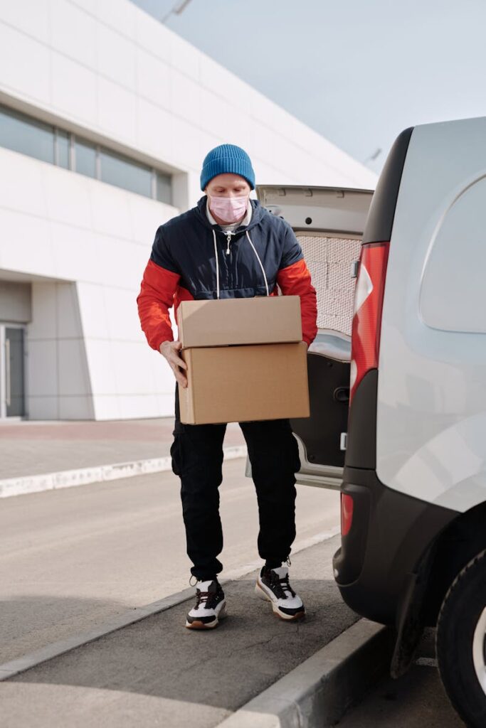 A delivery worker wearing a face mask unloading packages from a van in an urban area.