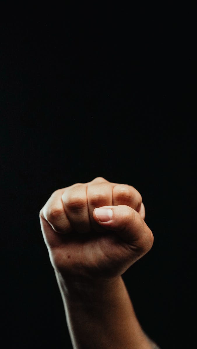 A powerful close-up of a fist raised in solidarity against a dark background, symbolizing strength and unity.