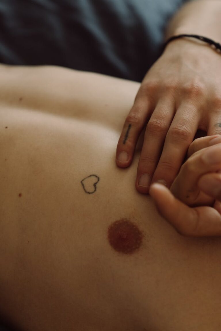 A close-up image of hands touching a lightly tattooed chest with an intimate vibe.
