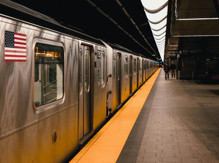 Image of a New York subway train at an underground station platform with an American flag.