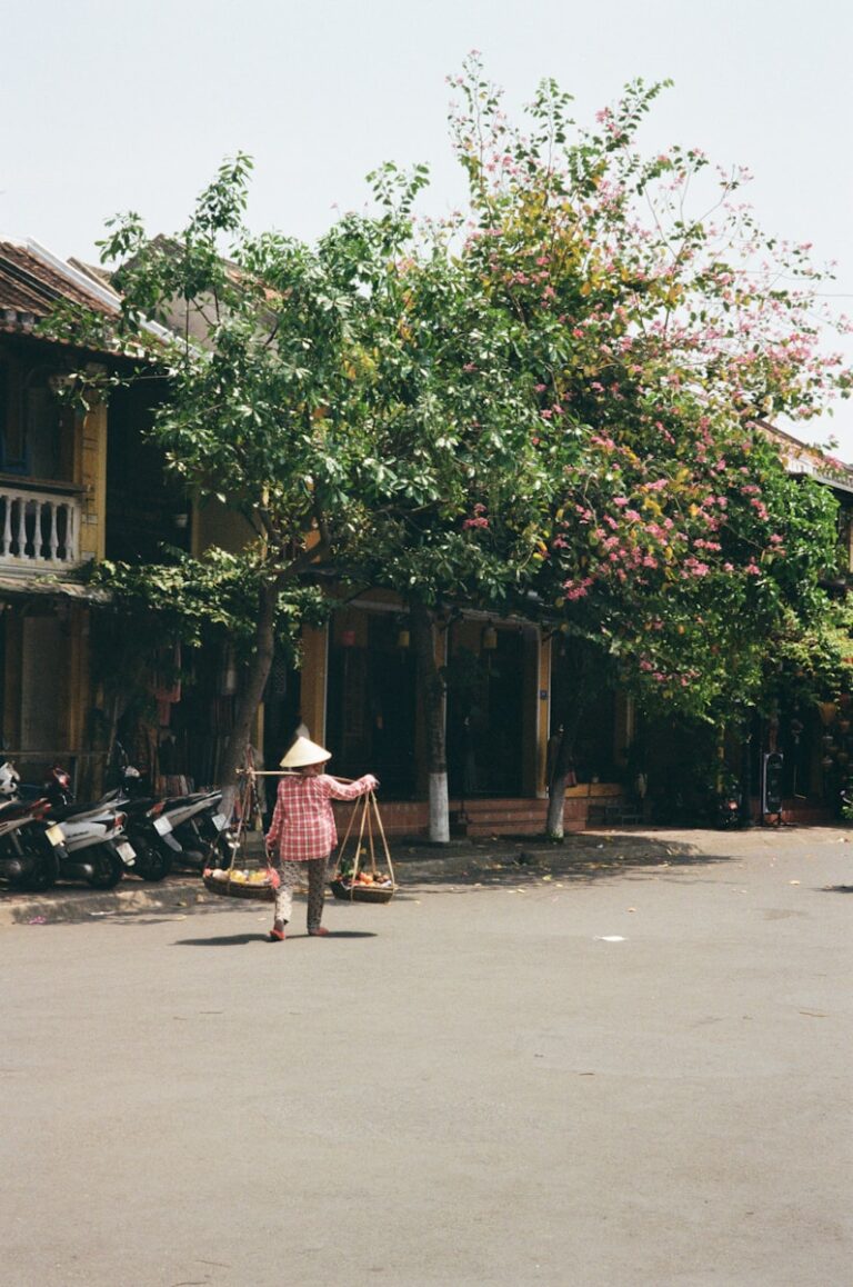 A woman walking down a street past a tree