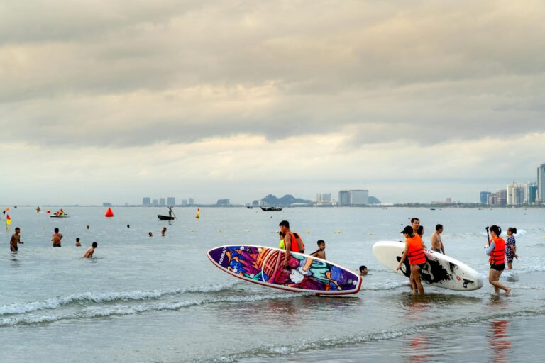 Group of people paddleboarding at a beach with city skyline in the background.