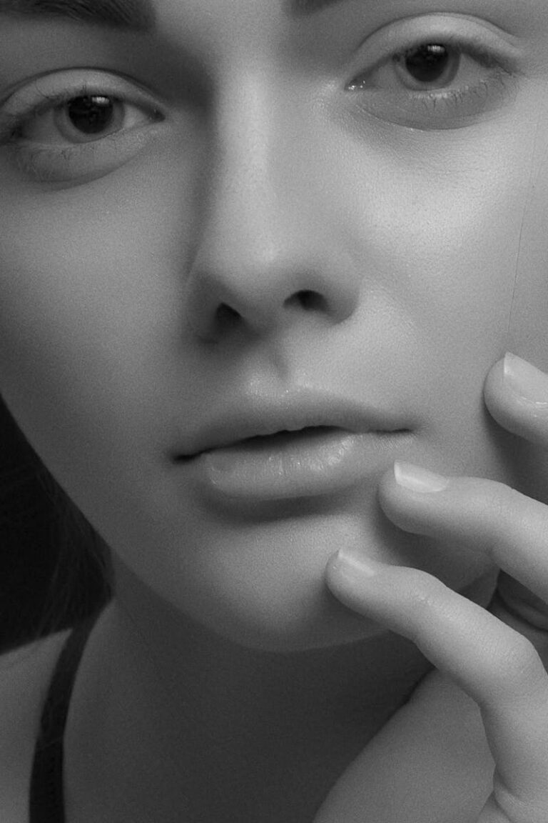 Close-up black and white portrait showcasing the beauty and elegance of a young woman's face with gentle hand placement.
