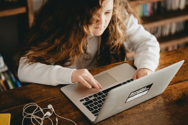 A woman in white long sleeve shirt using her laptop on brown wooden table