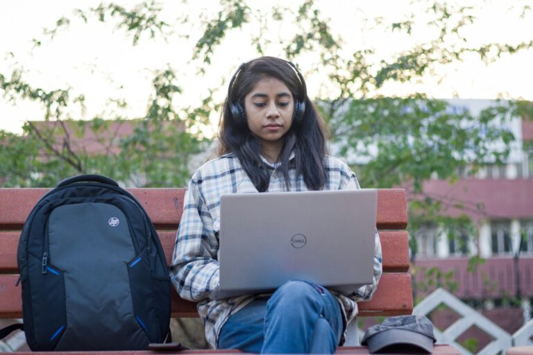 a young girl sitting on a bench using a laptop computer
