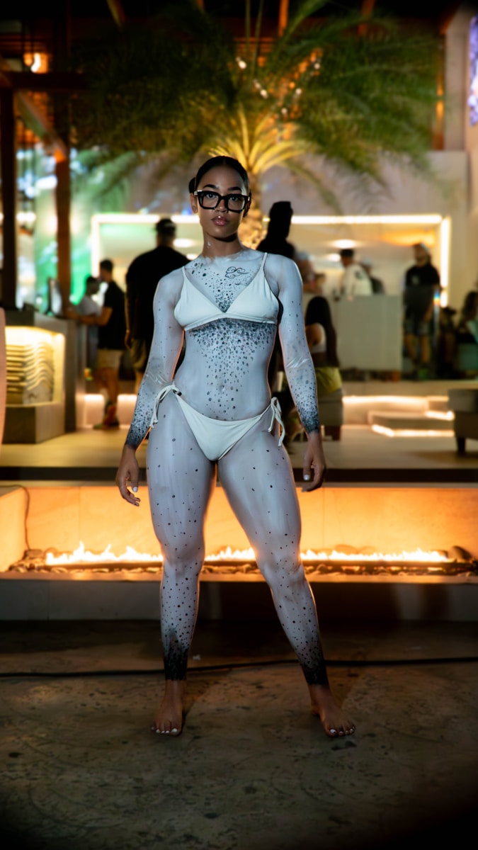 A young woman in a white bodysuit standing in front of a fire pit