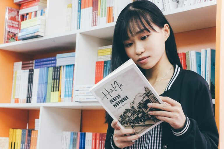 A young girl reading a book in front of a bookshelf