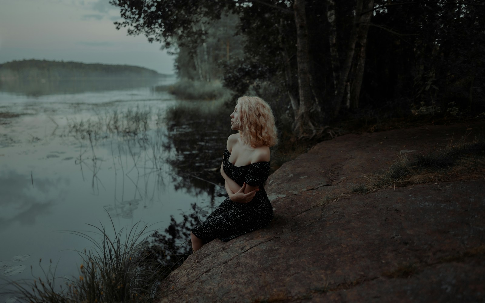A young woman sitting on a rock by a lake