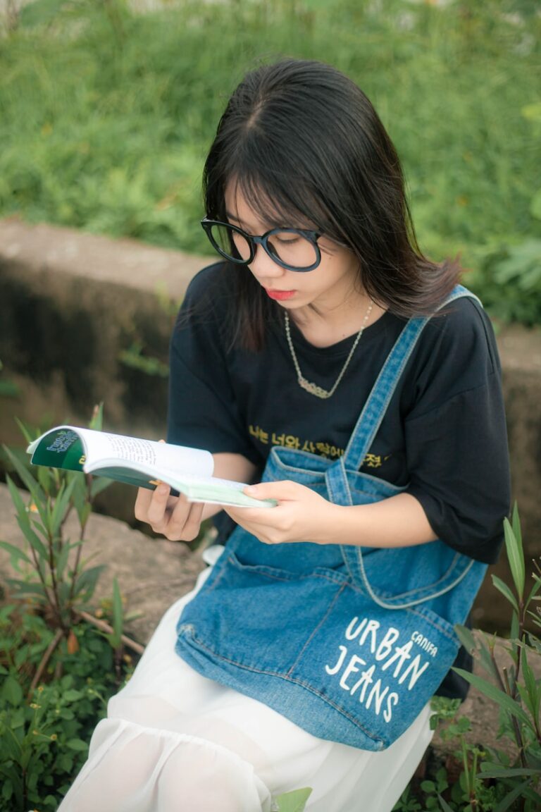 A woman in black crew neck shirt and blue denim jeans holding white book.