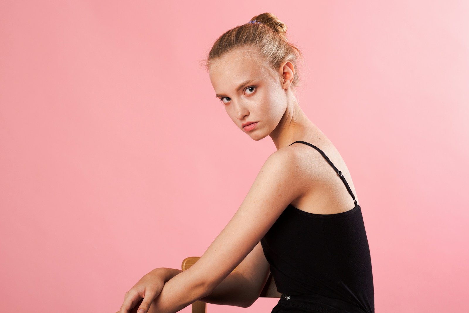 a woman sitting on a chair with a pink background