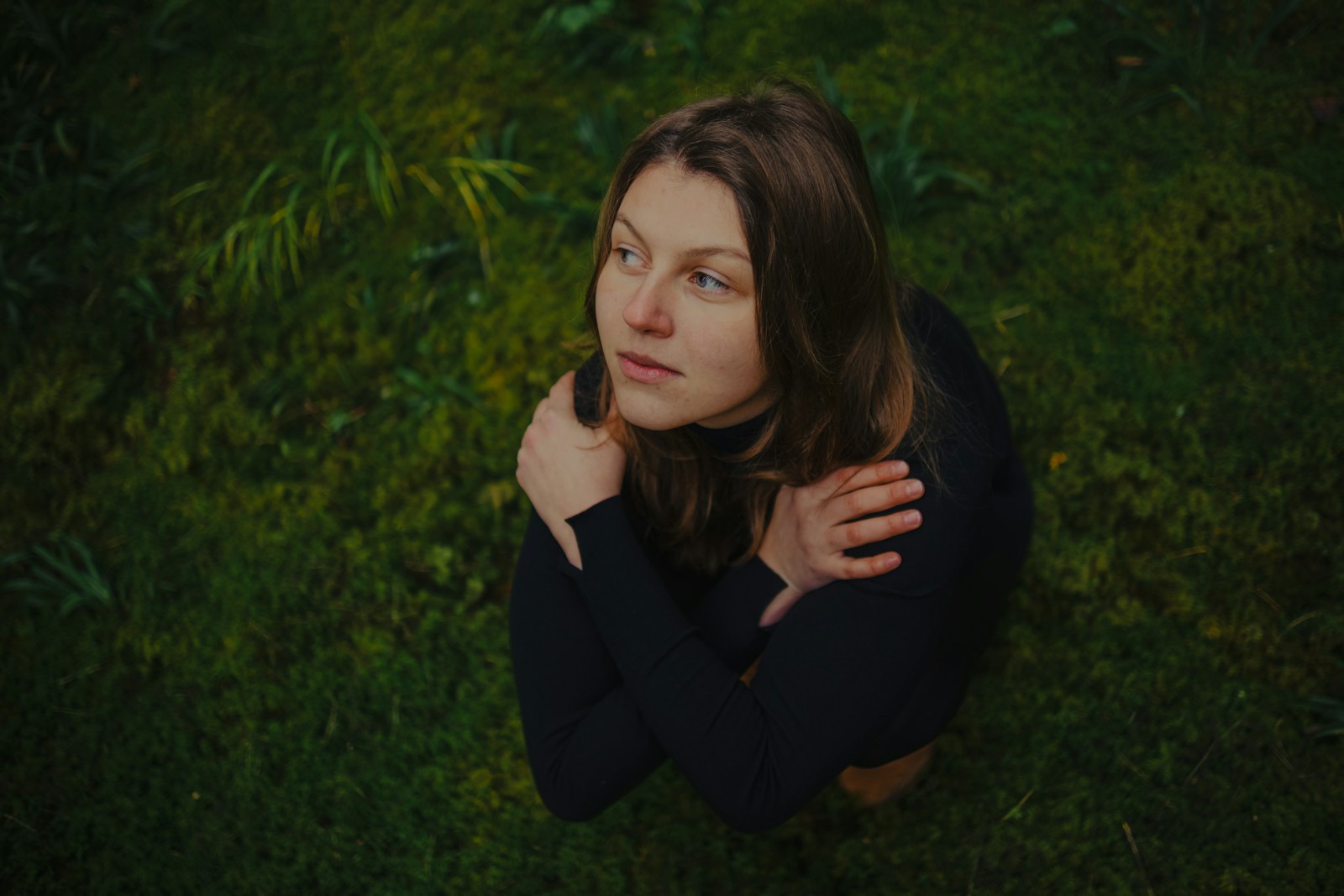 Young woman looking up thoughtfully in green foliage