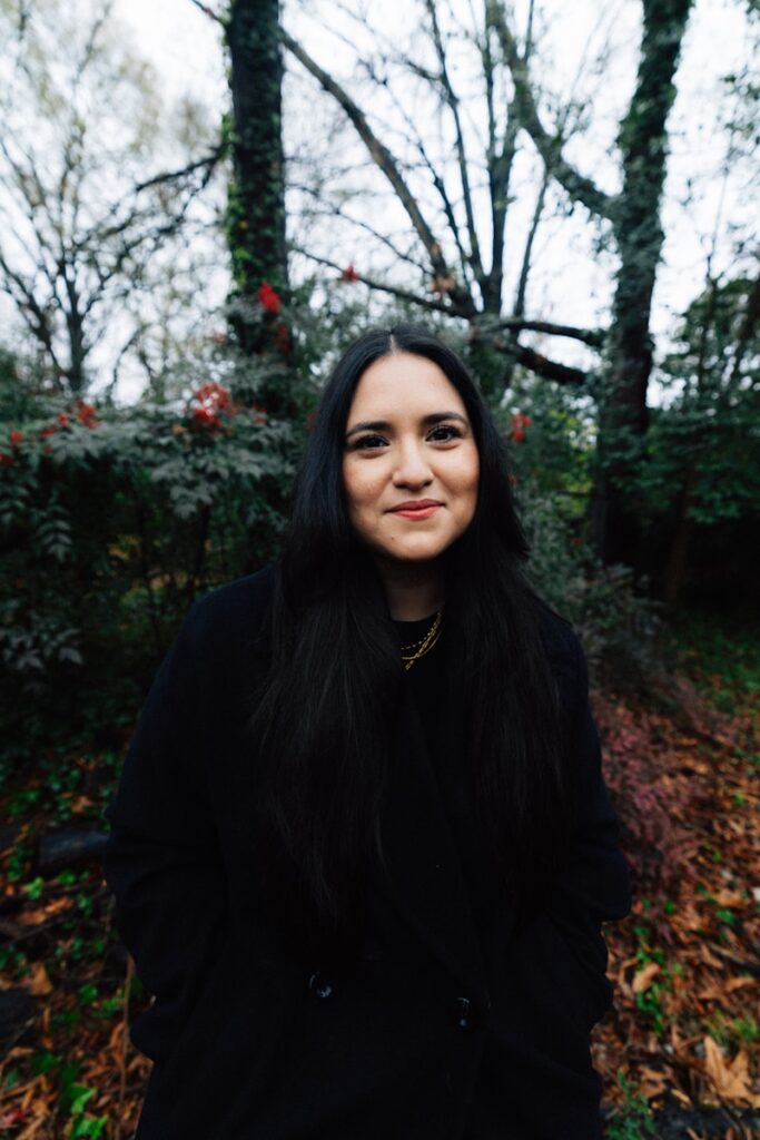 A woman with long dark hair smiles outdoors.